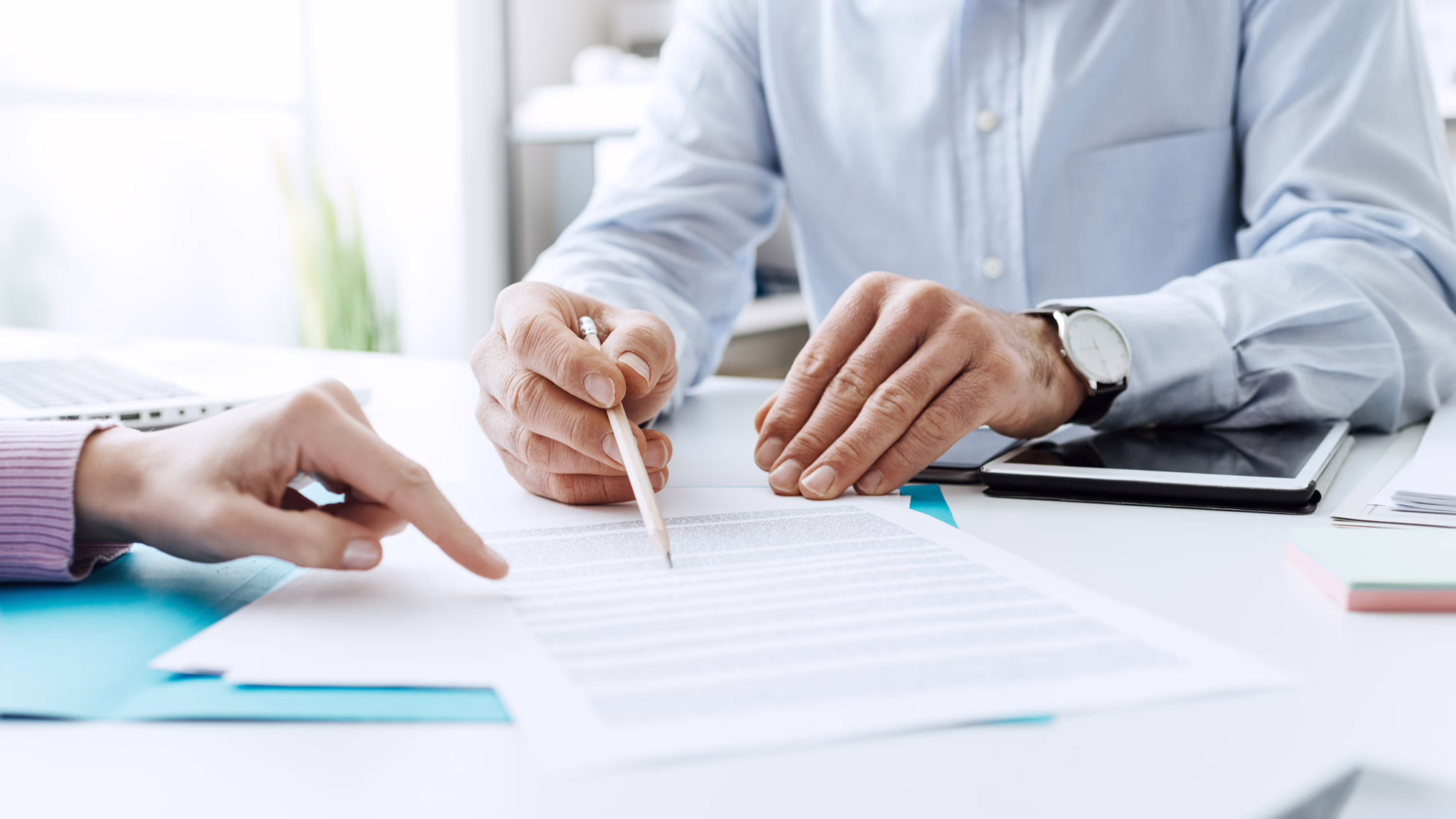 A person reviewing and signing paperwork at a desk with guidance from another individual.